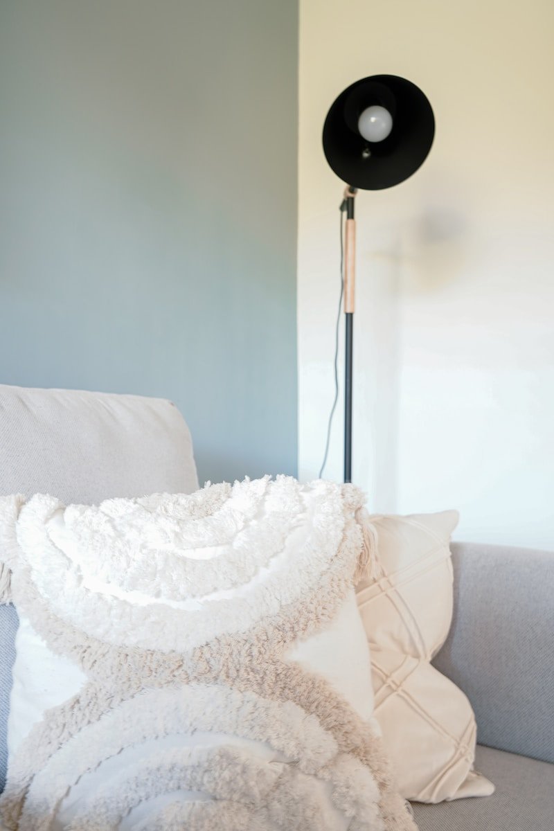 a white couch with a white pillow and a black floor lamp